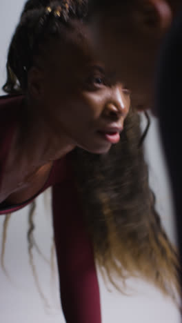 Vertical-Video-Studio-Shot-Of-Two-Women-Wearing-Gym-Fitness-Clothing-Facing-Each-Other-Exercising-1